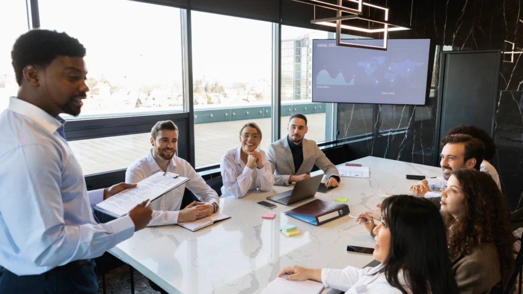 Business team in a meeting, a man presenting to colleagues seated around a large conference table.