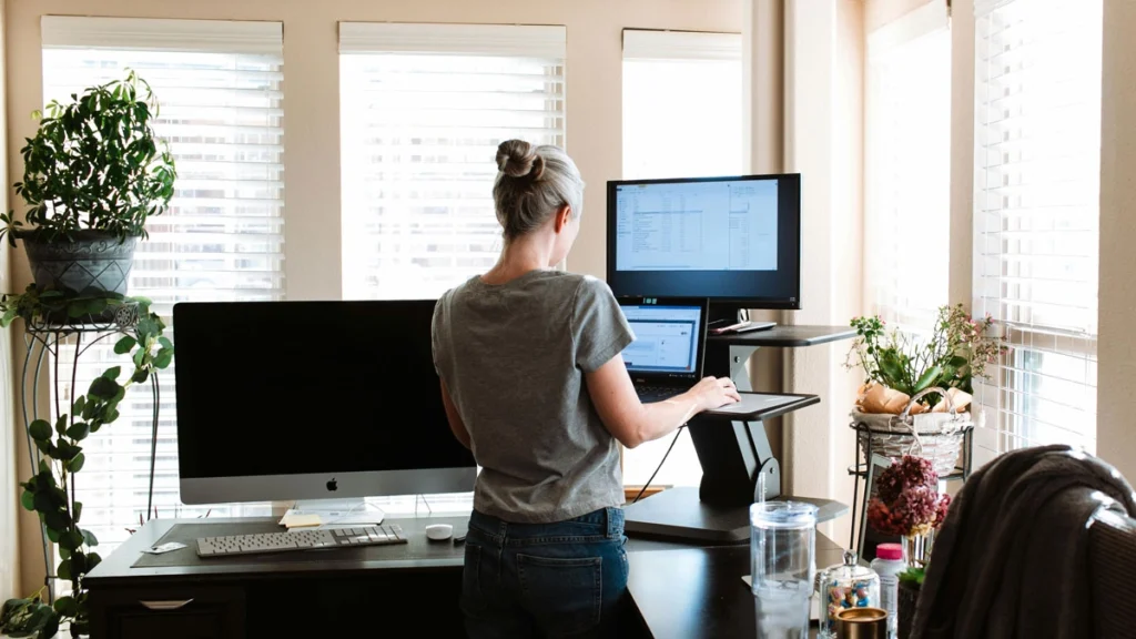 A woman stands at a desk, working on a computer, focused on her task in a well-lit office environment.